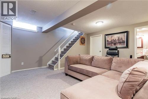 Finished lower level featuring light gray wall paint, light gray carpet flooring, a straight staircase with carpeted treads and white railings, and a white louvered door - 209 Auburn Drive Unit# A, Waterloo, ON 
