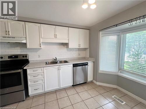 Kitchen featuring white cabinetry, subway tile backsplash, stainless steel appliances, a double basin sink, and a bay window - 209 Auburn Drive Unit# A, Waterloo, ON 