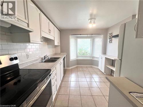Kitchen featuring white cabinetry, subway tile backsplash, stainless steel range, dual basin sink, and a bay window with blinds - 209 Auburn Drive Unit# A, Waterloo, ON 