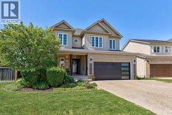 Two-story residence featuring light-colored siding and brick accents, a prominent front porch with dark support columns, a modern dark garage door with horizontal windows, a substantial exposed aggreg - 