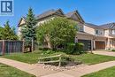 Exterior featuring light-toned siding and brick accents, a dark shingled roof, an attached garage with a modern dark door, a concrete sidewalk, and established landscaping with mature trees and shrubs - 61 Ditner Avenue, Baden, ON  - Outdoor 