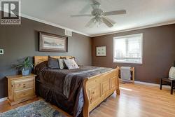 Bedroom featuring wood-finish flooring, a ceiling fan, crown molding, and a window with blinds - 