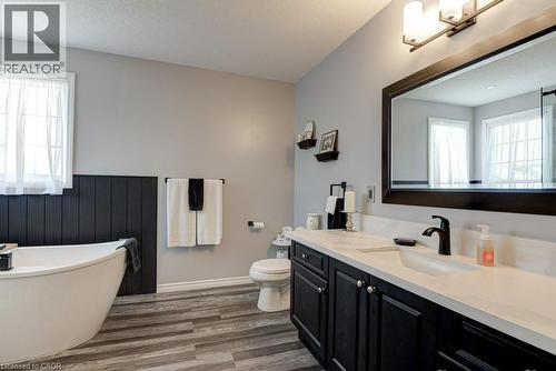 Bathroom featuring a freestanding tub, wood-finish flooring, a double vanity with a light-colored countertop, dark wood cabinetry, and a framed mirror - 61 Ditner Avenue, Baden, ON - Indoor Photo Showing Bathroom