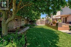 Expansive backyard featuring a lush lawn, mature trees, and a multi-level wood-finish deck - 