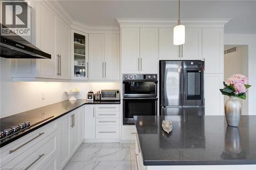 Contemporary kitchen featuring white cabinetry, dark countertops, integrated stainless steel appliances, a corner glass-front cabinet, and marble-look tile flooring - 57 Hollybrook Trail, Kitchener, ON 