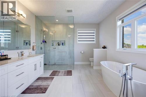 Contemporary bathroom featuring a freestanding tub, glass-enclosed shower, dual vanity with white cabinetry, light-toned tile flooring, and multiple windows - 57 Hollybrook Trail, Kitchener, ON 