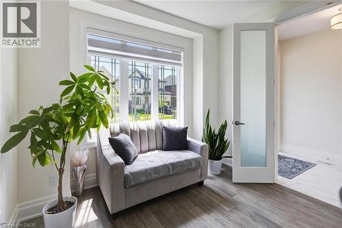 Bright interior space featuring a large window with grid detailing, wood-finish flooring, white baseboards, and a contemporary door with a frosted glass panel - 57 Hollybrook Trail, Kitchener, ON 