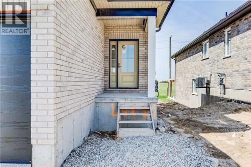 Main entrance featuring a covered porch with a white column, a light-colored entry door with windowpanes, and a concrete landing - 114 Bedell Drive, Mapleton, ON - Outdoor With Exterior
