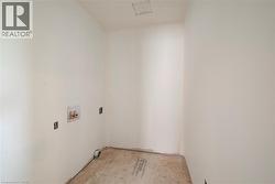 Dedicated utility space with white walls, rough plywood subfloor, and exposed plumbing connections - 