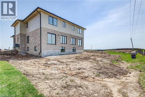 Two-story home with a light brick lower level and contrasting light siding on the upper level, featuring multiple windows with dark trim, a dark gutter system, and an exposed concrete foundation - 114 Bedell Drive, Mapleton, ON - Outdoor