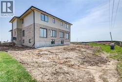 Two-story home with a light brick lower level and contrasting light siding on the upper level, featuring multiple windows with dark trim, a dark gutter system, and an exposed concrete foundation - 