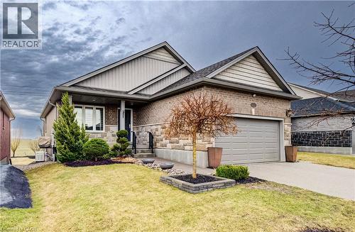 Single story home with a front lawn, driveway, a garage, a porch, and brick siding - 130 Bridge Crescent, Minto, ON 