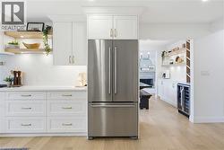 Modern kitchen featuring stainless steel appliances, white cabinetry with gold-tone hardware, and light wood-finish flooring - 