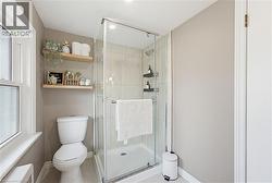 Full bathroom featuring a glass-enclosed shower with subway tile surround, white toilet, and dual wood-finish floating shelves - 