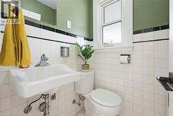 White square tile wainscoting with black accent trim, pedestal sink, toilet, and a window with privacy glass - 