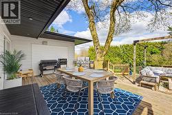 Expansive multi-level wood deck featuring a covered dining area, built-in recessed lighting, a privacy pergola, and mature landscaping - 