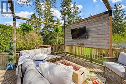 Expansive wood-decked patio featuring a slatted wood privacy wall with mounted television, a built-in fire pit, and a pergola structure - 