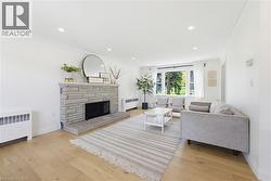 Living area featuring a stone-clad fireplace, wood-finish flooring, recessed lighting, crown molding, and a bay window - 