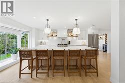 Spacious kitchen featuring a large central island with seating, a bay window, wood-finish flooring, white cabinetry, and stainless steel appliances - 