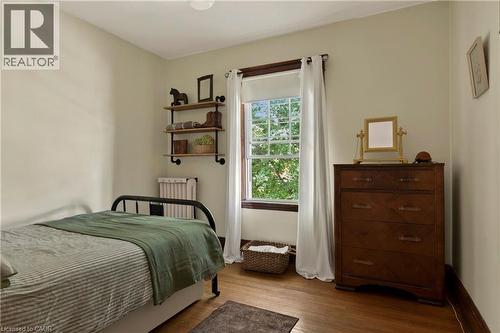 Warm-toned wood-finish flooring provides a rich base for this room featuring a window with white trim, offering natural light - 111 Spadina Avenue, Hamilton, ON 