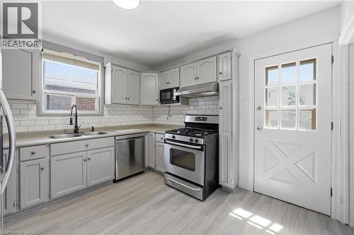 Kitchen featuring light gray cabinetry, white subway tile backsplash, stainless steel appliances, and wood-finish flooring - 97 Tragina Avenue S, Hamilton, ON 