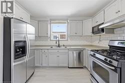 Kitchen featuring light-finish cabinetry, stainless steel appliances, subway tile backsplash, light-toned countertops, and wood-finish flooring - 