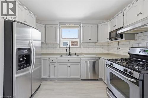 Kitchen featuring light-finish cabinetry, stainless steel appliances, subway tile backsplash, light-toned countertops, and wood-finish flooring - 97 Tragina Avenue S, Hamilton, ON 