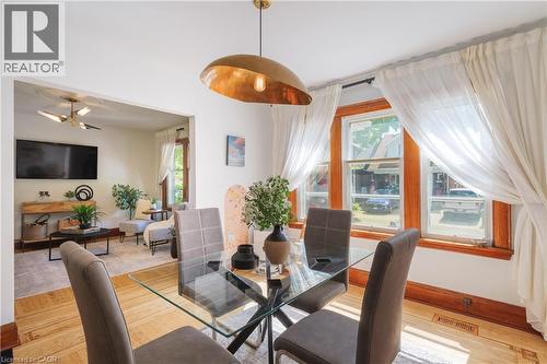 Dining area featuring a contemporary brass pendant light, wood-finish flooring, and a glass-top table - 41 Park Row N, Hamilton, ON 