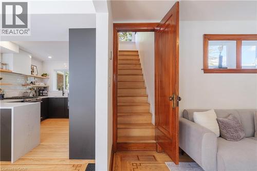 Hardwood staircase with a solid wood door, featuring a kitchen with a waterfall island, white subway tile backsplash, and floating shelves - 41 Park Row N, Hamilton, ON 