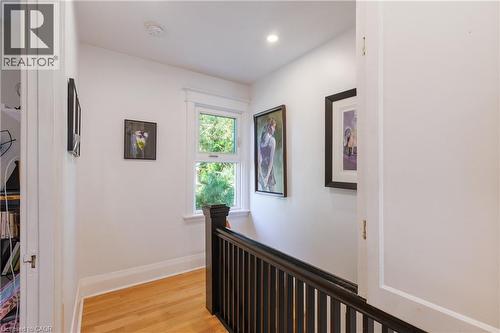 Hallway featuring wood-finish flooring, white walls, and a white trim window overlooking greenery - 41 Park Row N, Hamilton, ON 