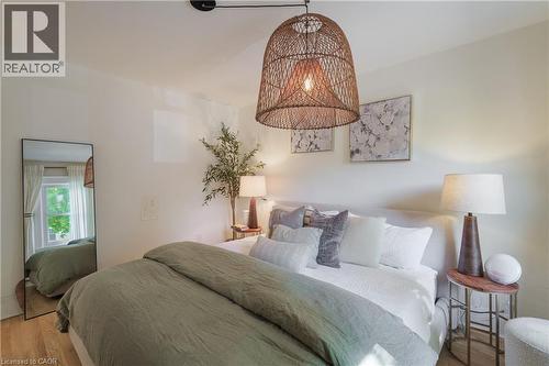 Bedroom featuring wood-finish flooring, a woven pendant light fixture, and a window with natural light - 41 Park Row N, Hamilton, ON 