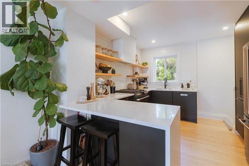 Modern kitchen featuring a waterfall island with counter seating, black base cabinetry, open wood shelving, a white subway tile backsplash, and light wood-finish flooring - 41 Park Row N, Hamilton, ON 