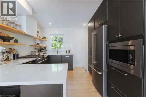 Modern kitchen featuring a white countertop island, dark cabinetry, and light wood-finish flooring - 41 Park Row N, Hamilton, ON 