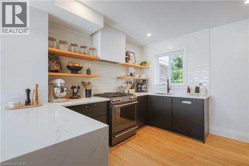 Modern kitchen featuring light wood-finish flooring, dark cabinetry, and white quartz countertops - 41 Park Row N, Hamilton, ON 