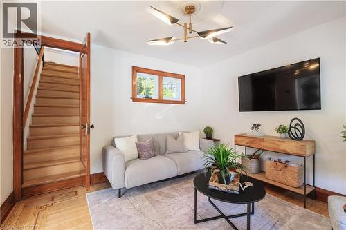 Bright living area with hardwood flooring featuring a decorative inlay, a modern ceiling light fixture, and white wall finishes - 41 Park Row N, Hamilton, ON 