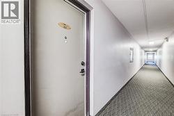 Entry door with dark trim and hardware, positioned within a carpeted hallway featuring overhead lighting and wall-mounted fixtures - 