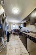 Galley kitchen with dark wood-finish cabinetry, stainless steel appliances, and light-toned tile flooring - 
