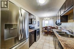 Kitchen featuring stainless steel appliances, dark wood-finish cabinetry, a tile backsplash, and light-toned countertops - 