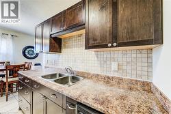 Kitchen featuring dark wood-finish cabinetry, a double basin stainless steel sink, speckled laminate countertops, and a tiled backsplash - 