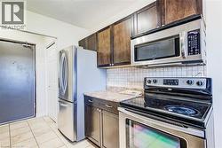 Kitchen featuring stainless steel appliances, dark wood-finish cabinetry, and a light-toned countertop - 