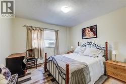 Bedroom featuring wood-finish flooring, a window with blinds and curtains, and a ceiling-mounted light fixture - 