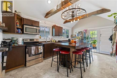 Kitchen featuring a vaulted ceiling with exposed beams, central island with seating, stainless steel appliances, white subway tile backsplash, and double glass-paneled doors with louvered shutters - 54 E Chestnut Street E, St. Catharines, ON - Indoor Photo Showing Kitchen