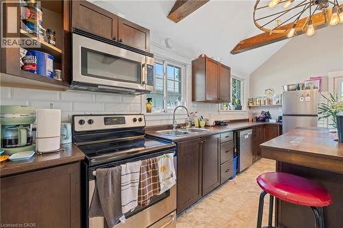 Kitchen featuring wood-finish cabinetry, stainless steel appliances, a double basin sink, white subway tile backsplash, and vaulted ceilings with exposed wood beams - 54 E Chestnut Street E, St. Catharines, ON - Indoor Photo Showing Kitchen With Double Sink