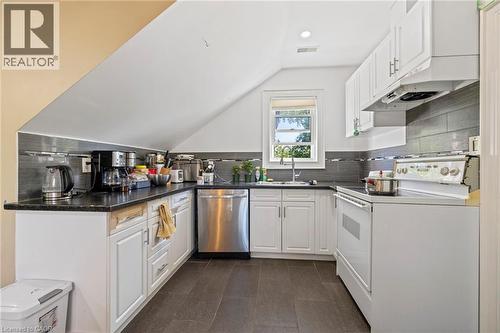 Modern kitchen featuring white cabinetry, dark countertops, dark tile backsplash, stainless steel dishwasher, and a window above the sink - 54 E Chestnut Street E, St. Catharines, ON - Indoor