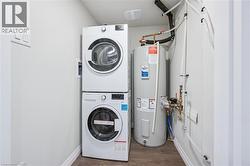 Washroom with dark wood-style flooring, electric water heater, and estacked washer and dryer - 