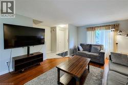 Living area with wood-finish flooring, light grey wall paint, and a large window with privacy coverings - 