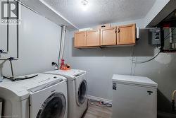 Dedicated laundry area featuring wood-finish overhead cabinetry, light gray walls, and wood-finish flooring - 