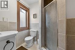 Bathroom featuring a tiled shower enclosure with textured glass, ceramic tile wainscoting, and a wood-framed window - 
