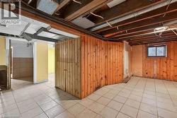 Open floor plan basement featuring exposed ceiling joists, wood-paneled walls, and ceramic tile flooring - 