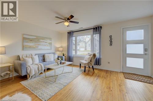 Bright living area featuring wood-finish flooring, a modern front entry door with frosted panels, and a large window with sheer drapes - 73 East 33Rd Street, Hamilton, ON 